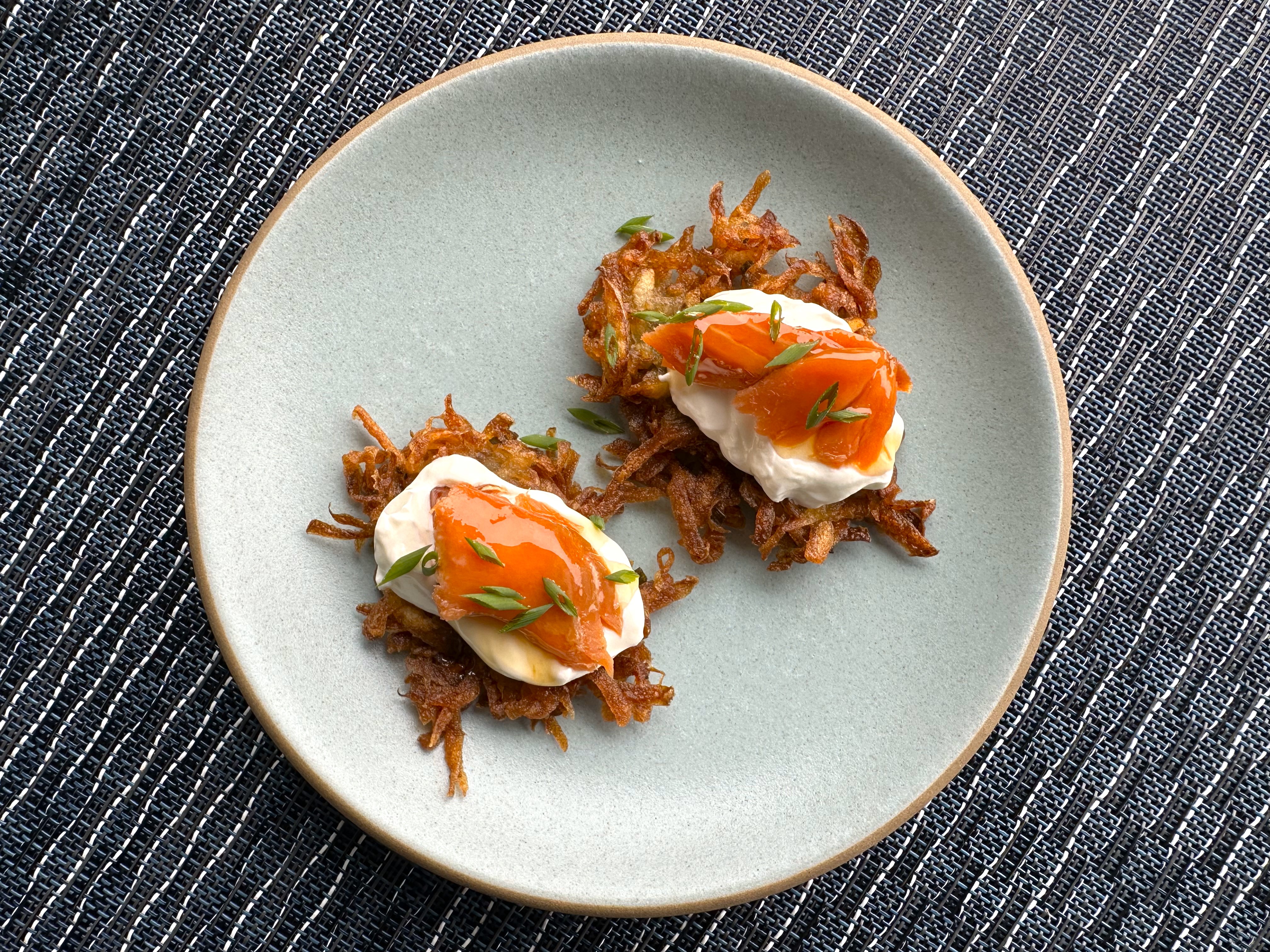 A plate with two mini latkes topped with salmon and sour cream